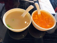 两碗汤,白色瓷碗,一碗浅色,一碗橙色,配有汤勺,桌子。