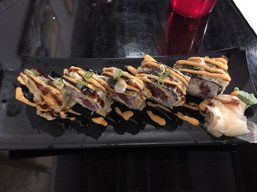 寿司卷美食,摆放在黑色盘子上,佐以酱汁,顶部装饰。美食图片,美味寿司。