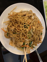 盘子里的炒面,配有蔬菜和肉,旁边有筷子和叉子。